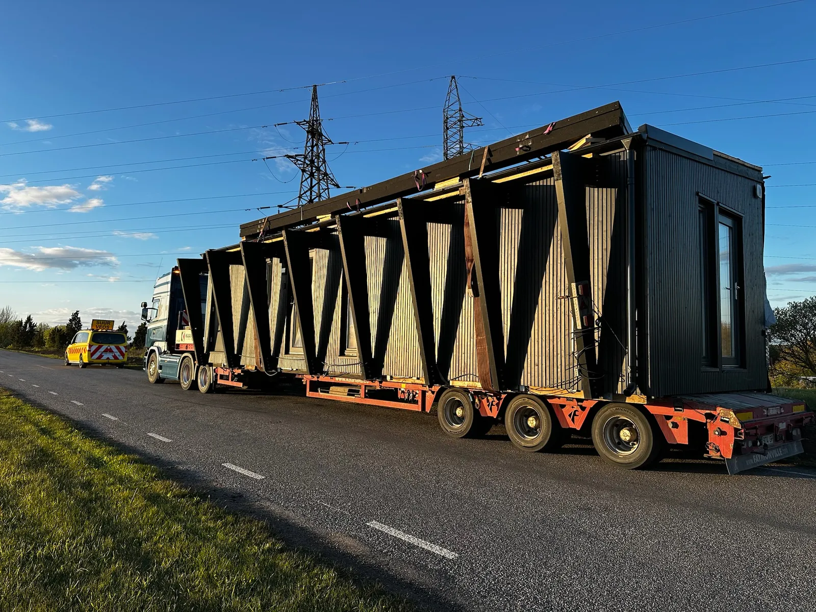 A finished Corner House module on a low-loader trailer being delivered by road at sunset